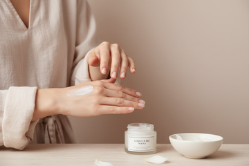 minimalist beauty photography of a woman gently massaging cream into her hands, clean natural nails, smooth skin, simple neutral clothing, plain pastel nude background, soft blush and ivory tones, calm spa mood, woman performing hand care ritual, luxury hand and foot care brand aesthetic, high resolution website wallpaper
